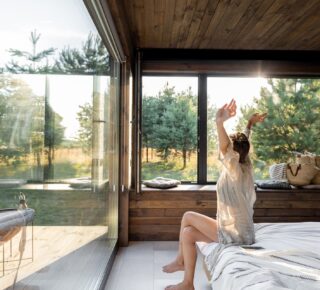 Vrouw rekt zich uit. Ze zit op de hoek van haar bed in een vakantiehuisje in Zeeland.