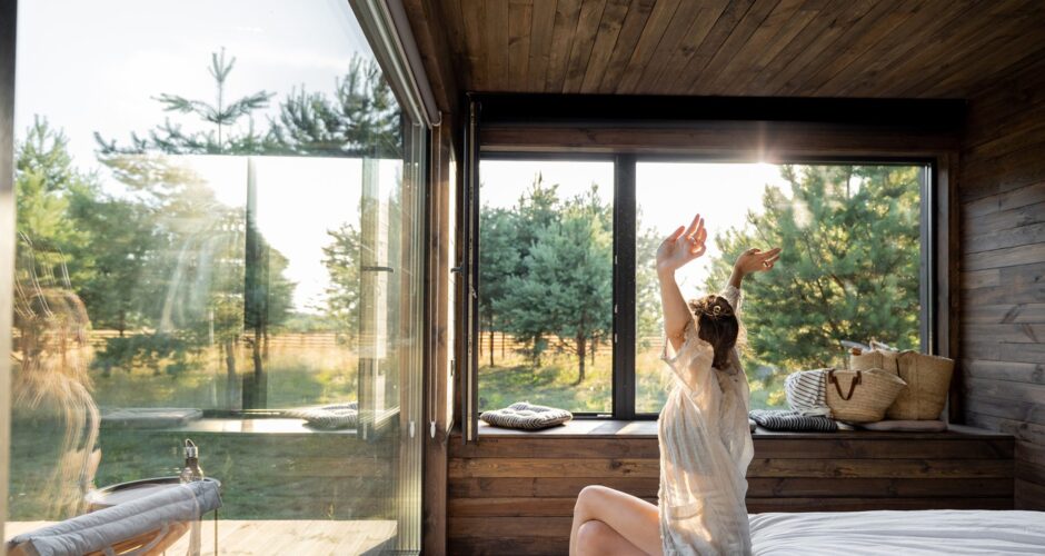 Vrouw rekt zich uit. Ze zit op de hoek van haar bed in een vakantiehuisje in Zeeland.